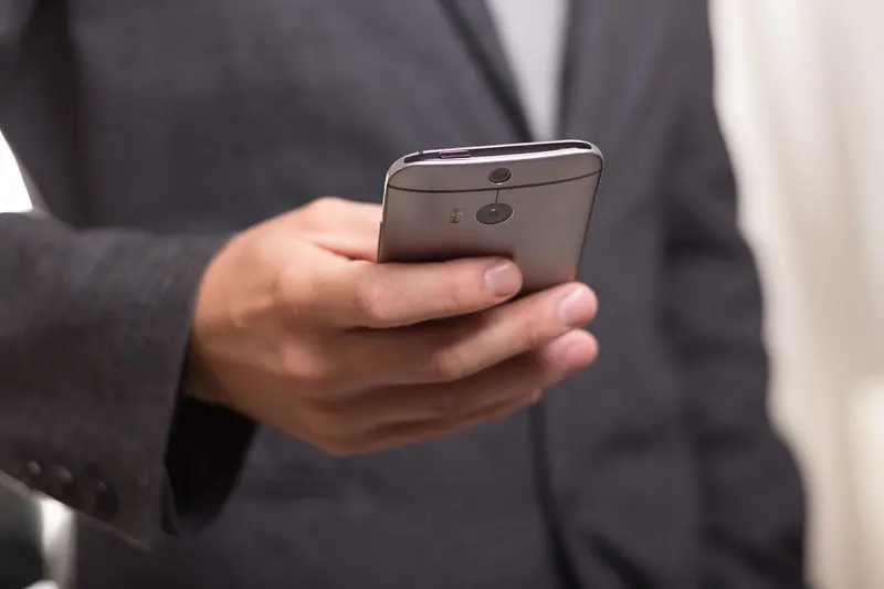Mão de um homem de blazer segurando o celular, sem o rosto aparecer
