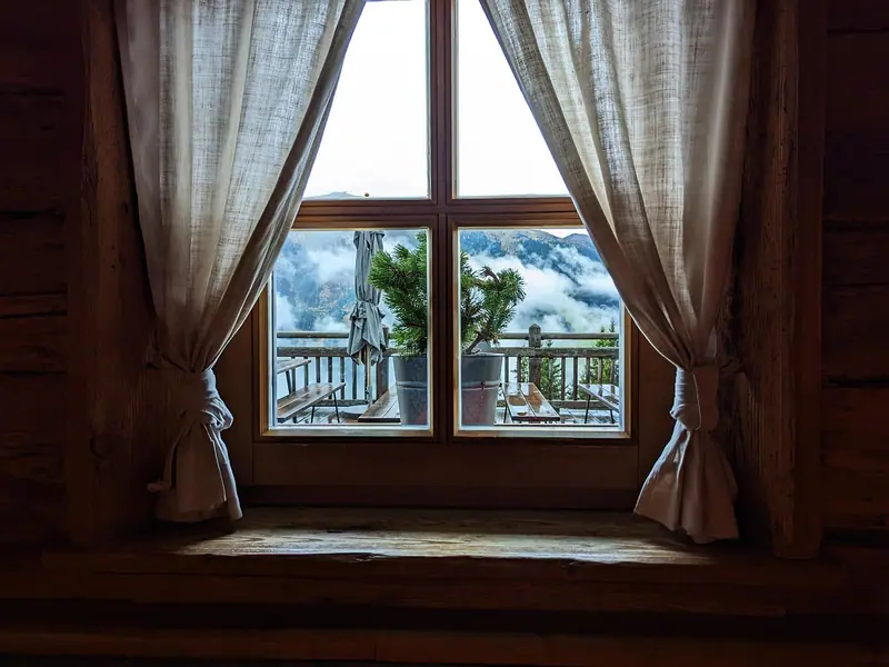 Cortinas claras presas dos dois lados de uma janela de madeira, com uma varanda do lado de fora