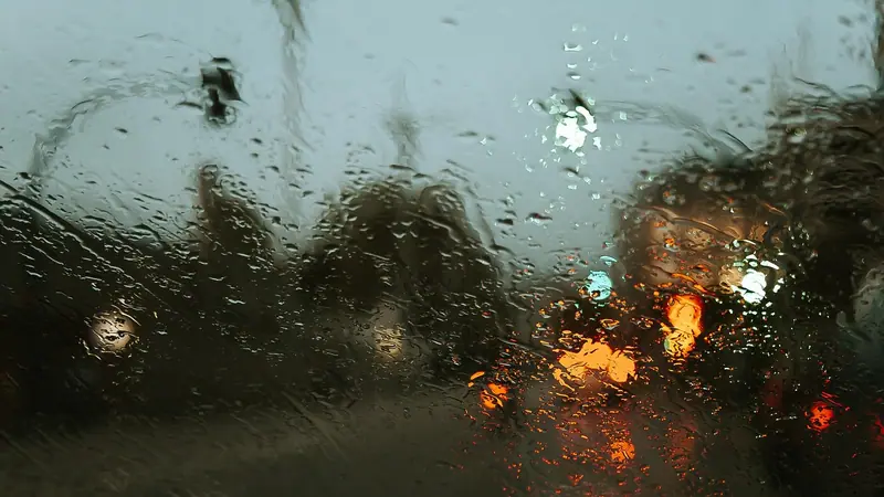 Gotas de chuva num vidro de janela, com faróis e luzes da rua desfocados do lado de fora