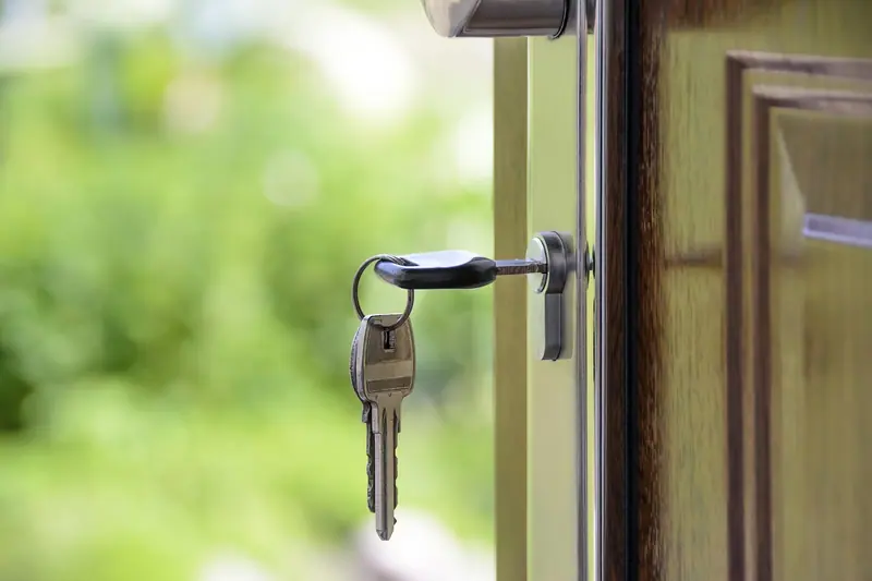 Chave com chaveiro encaixada na fechadura de uma porta de madeira entreaberta