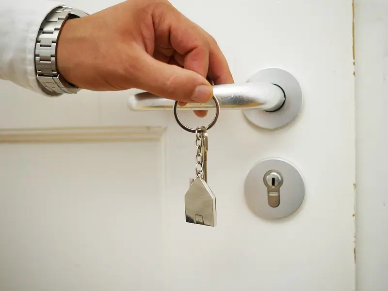 Mão segurando um molho de chaves junto à maçaneta de uma porta branca