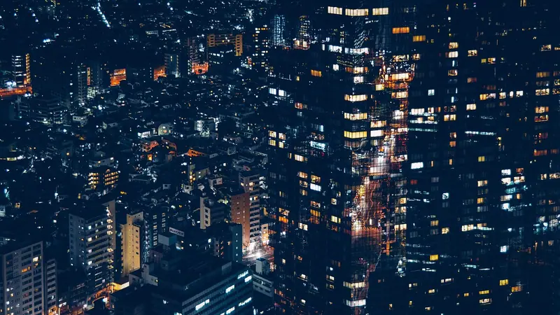 Vista do alto de uma cidade à noite, com muitos prédios iluminados e ruas acesas