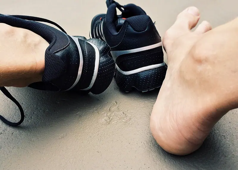 Par de tênis esportivos pretos ao lado de um pé descalço apoiado no chão