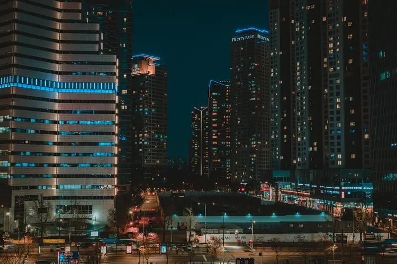 Prédios altos iluminados à noite, com avenidas e luzes da cidade em primeiro plano