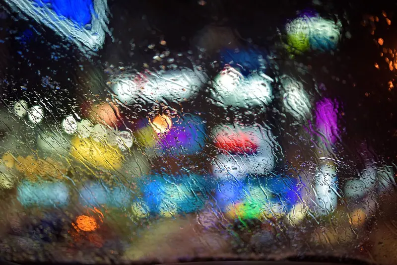 Luzes coloridas da cidade à noite, desfocadas atrás de um vidro com gotas de chuva
