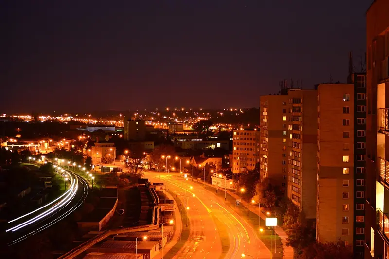 Avenida iluminada por luzes alaranjadas à noite, ao lado de prédios residenciais