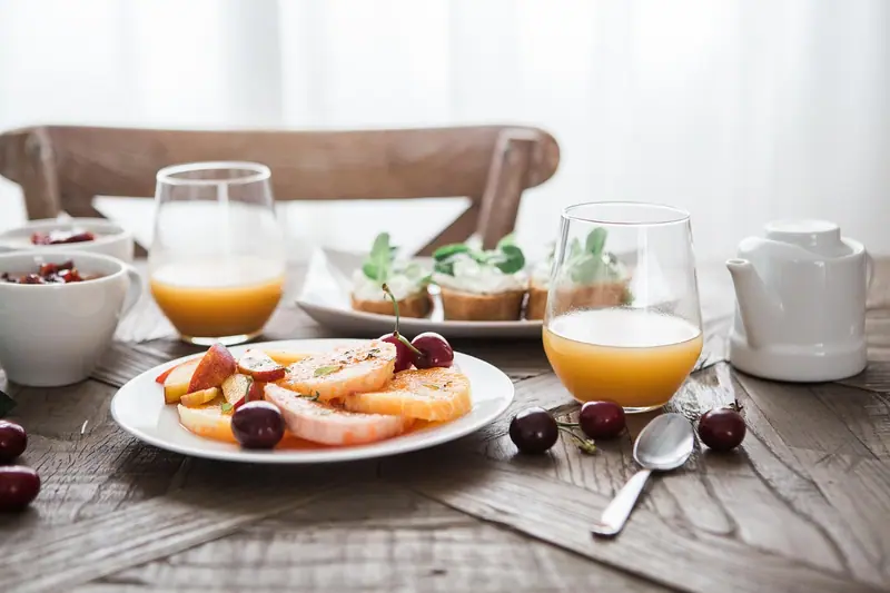 Mesa de café da manhã com frutas fatiadas, sucos e doces, sob a luz do dia