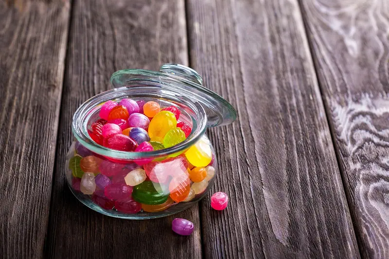 Pote de vidro aberto com balas de goma coloridas sobre uma mesa de madeira