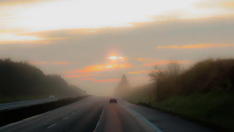 Estrada de várias faixas com neblina ao amanhecer e poucos carros ao longe