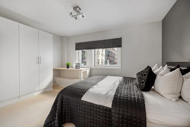 Quarto claro com cama de casal arrumada, almofadas, armário branco e janela com persiana