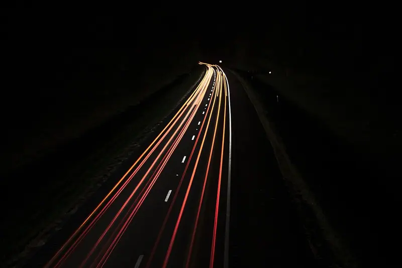 Rastros de luz de faróis numa estrada escura à noite, em foto de longa exposição
