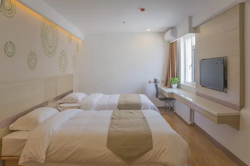 Quarto com camas arrumadas, uma bancada de trabalho e um ar-condicionado split na parede, ao lado da janela