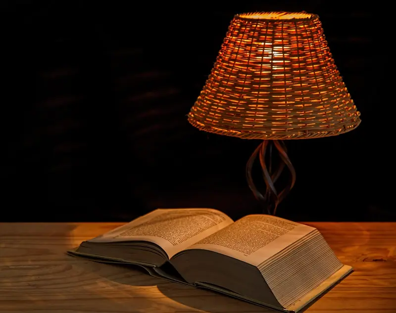 Abajur de palha aceso sobre uma mesa de madeira, iluminando um livro aberto