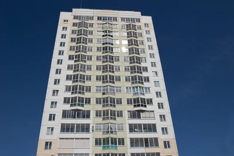 Prédio residencial alto, com muitas janelas e varandas, contra um céu azul