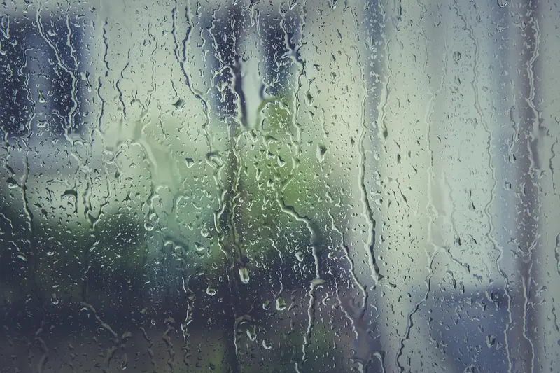Gotas de chuva escorrendo num vidro de janela, com a paisagem desfocada ao fundo