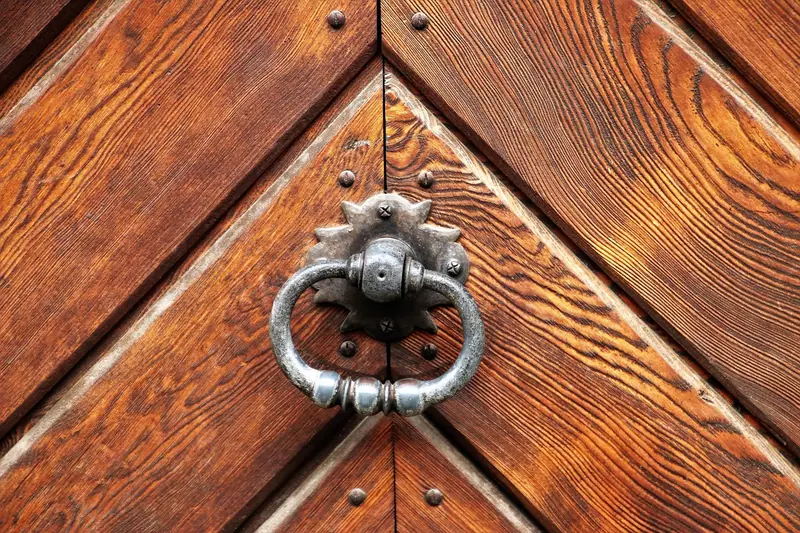 Porta de madeira com tábuas em diagonal e uma argola de metal escuro no centro