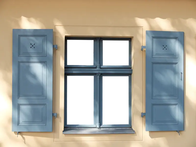 Janela com venezianas de madeira azul-claras abertas numa fachada amarela