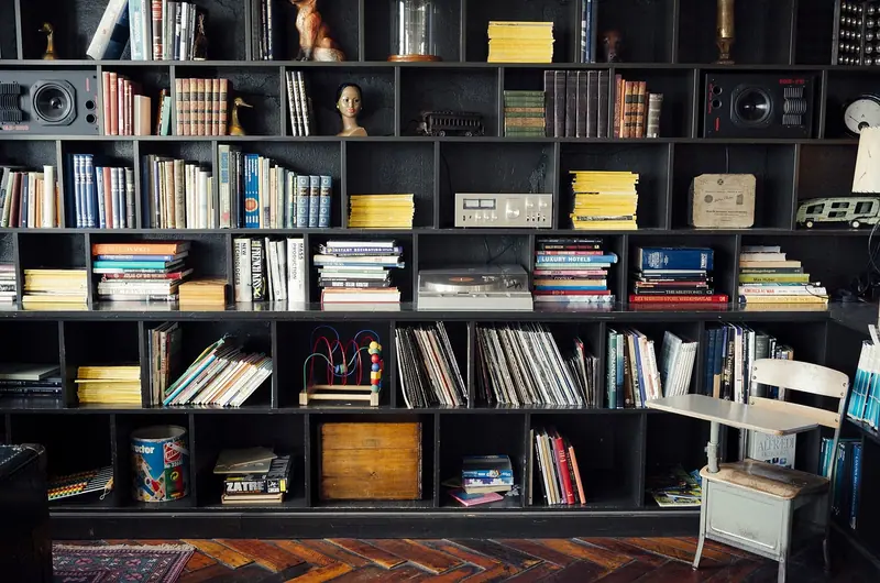Estante alta cheia de livros e objetos ocupando a parede inteira de uma sala