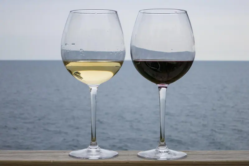 Duas taças de vinho sobre um parapeito, com o mar e o céu ao fundo